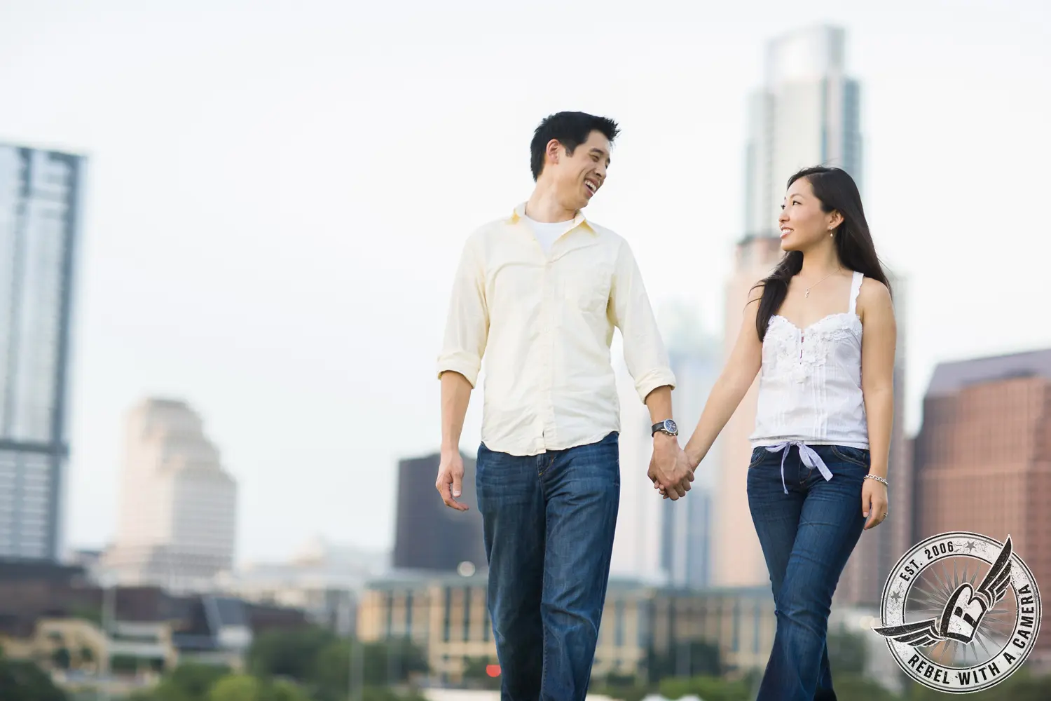 Couple walking hand in hand with a city skyline behind them in Austin, TX.