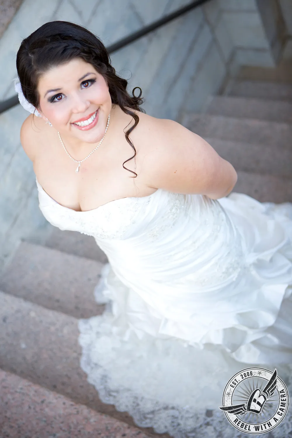 Smiling bride in a white wedding dress photographed from above on stone steps