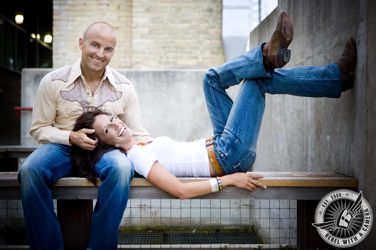 Playful couple posing on a bench with one person resting their legs against a wall