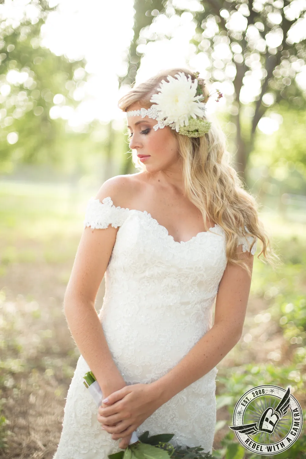 Bride in a white lace dress with a large flower headpiece standing in a sunlit wooded setting in Austin, TX.