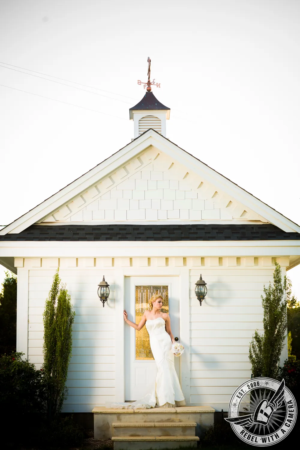 Bride in a white dress holding a bouquet in front of a small white chapel