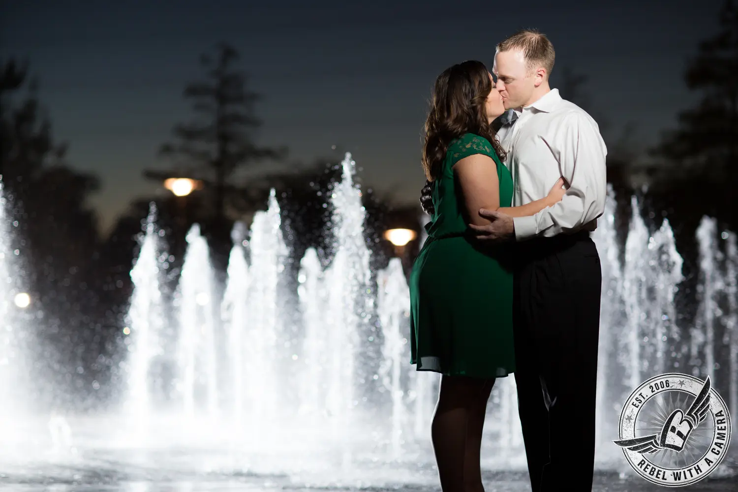 Couple kissing in front of illuminated fountains at night in Austin, TX.