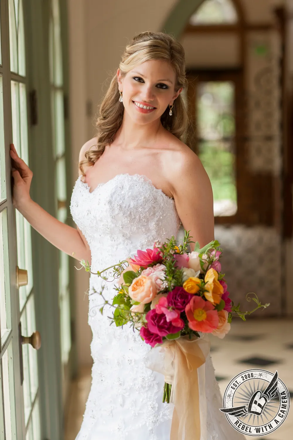 Smiling bride in a white wedding dress holding a colorful bouquet in a doorway in Austin, TX.