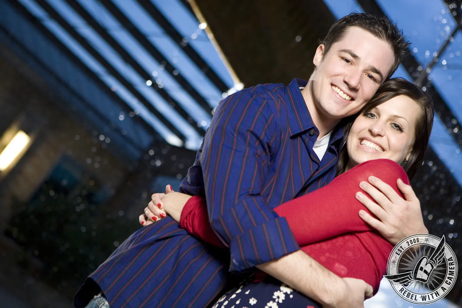 Smiling couple posing closely together beneath a modern glass structure