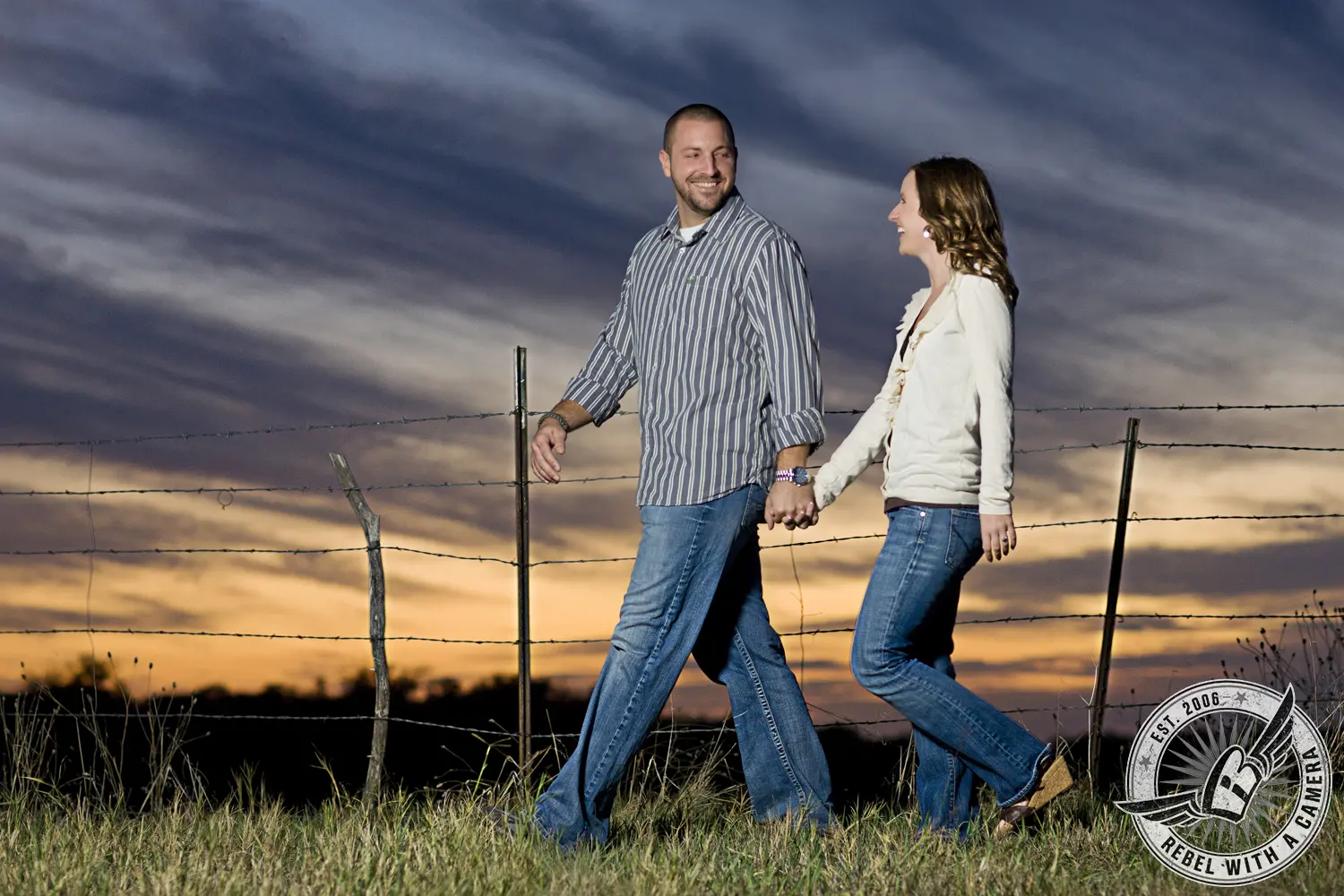 Couple walking hand in hand beside a barbed wire fence at sunset