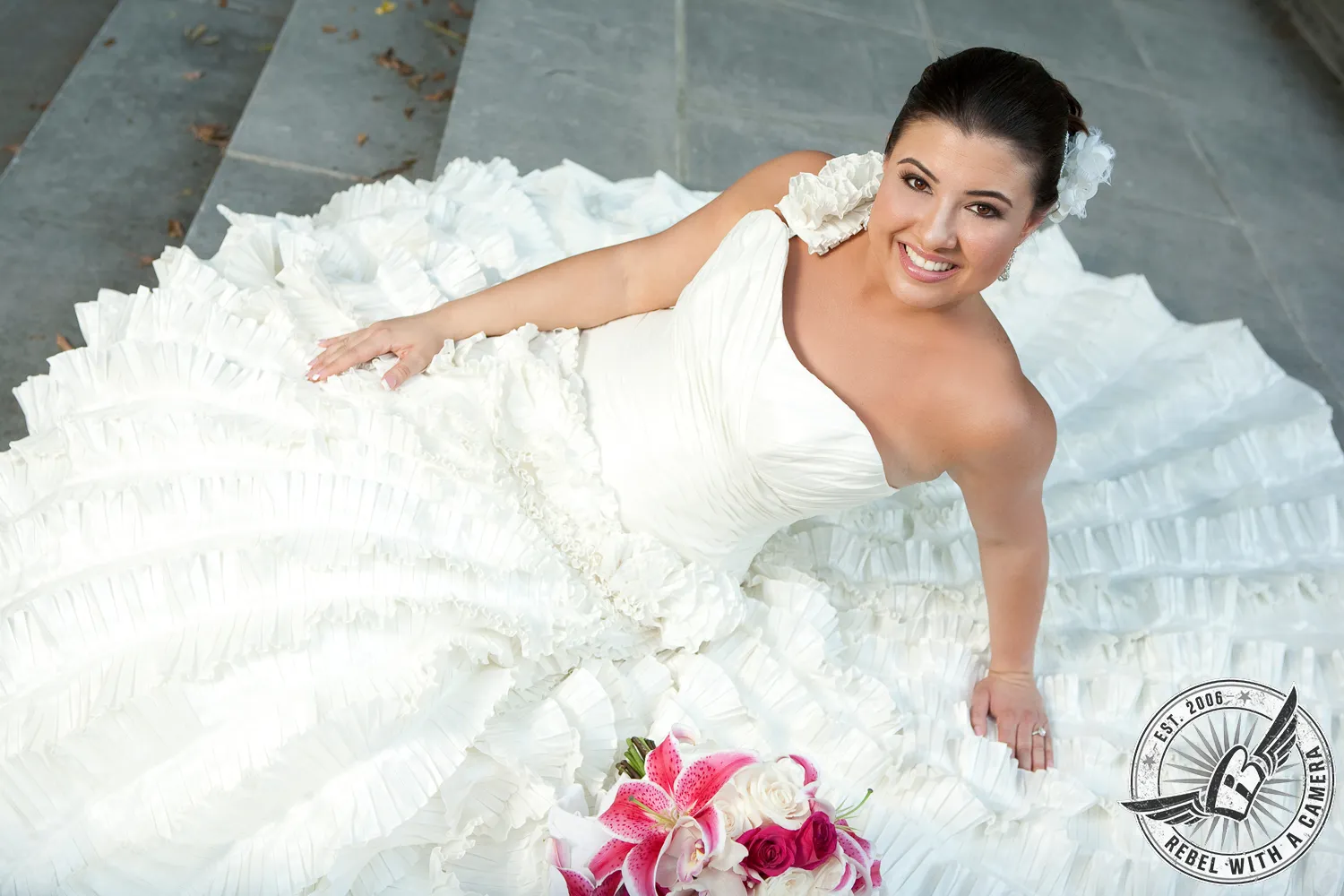 Smiling bride reclining in a ruffled wedding dress with a pink bouquet in Austin, TX.