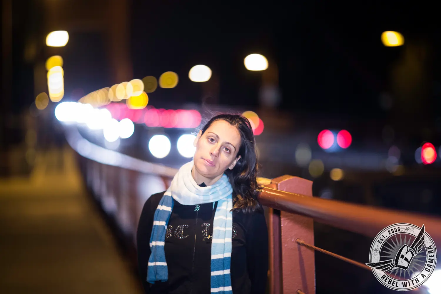 Woman posing on a city bridge at night with blurred lights behind her in Austin, TX.