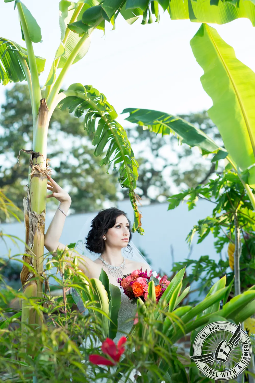 Bride holding a colorful bouquet among tropical banana leaves in Austin, TX.
