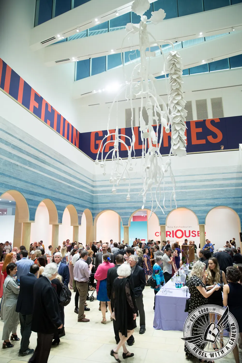 Guests gather beneath a large white hanging sculpture in the Blanton Museum of Art atrium during the Curiouser exhibit event.