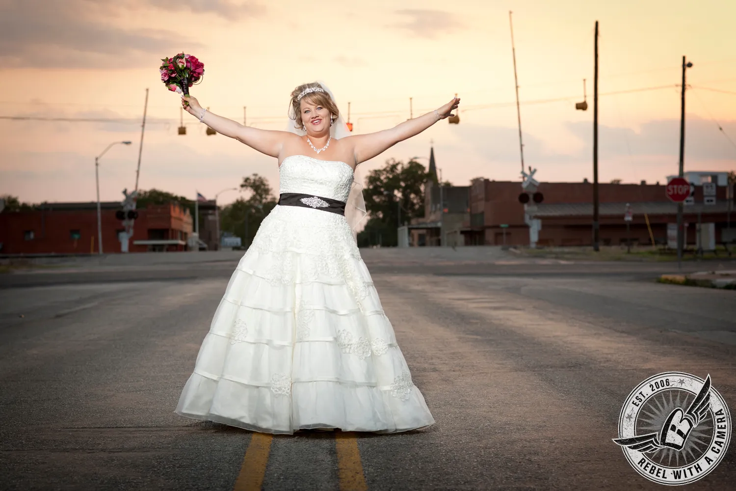 Bride standing in the middle of a street at sunset with her bouquet raised in Austin, TX.