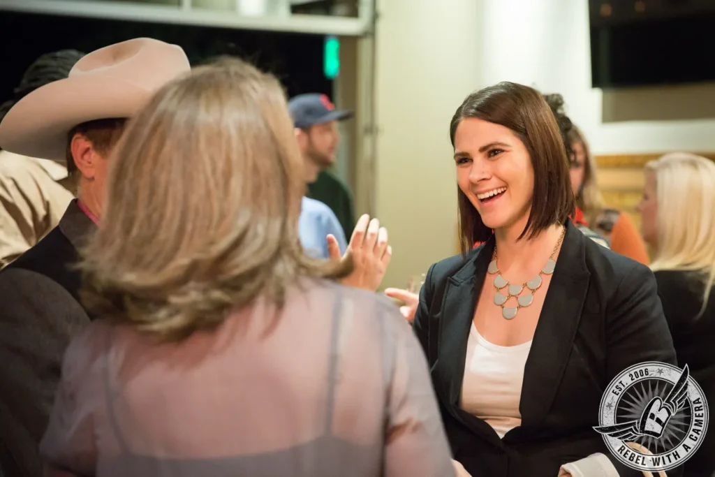 Smiling woman in a black blazer speaking with event guests in Austin, TX.