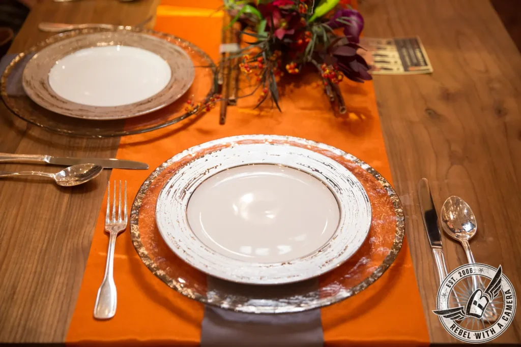 Formal event place setting with orange table runner and floral centerpiece
