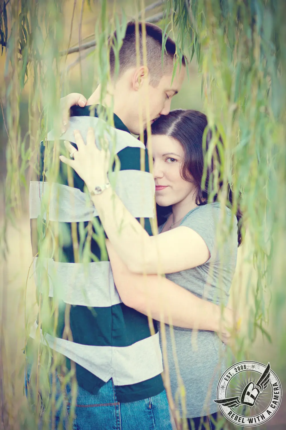 Couple embracing beneath hanging willow branches in Austin, TX.