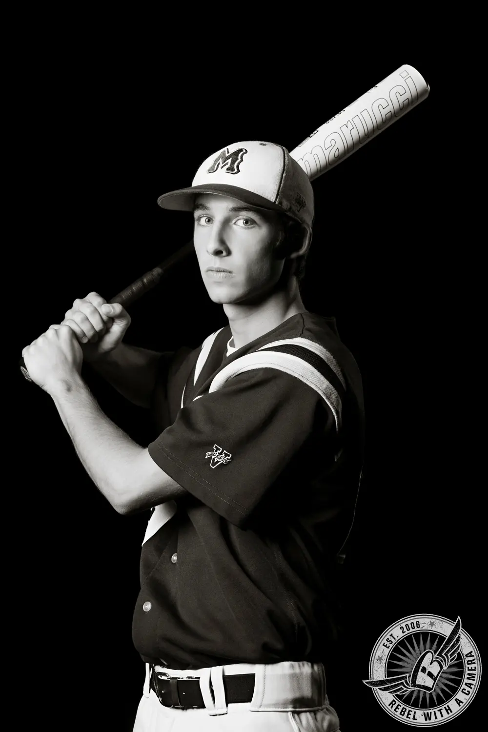 Black-and-white portrait of Jacob in a baseball uniform holding a bat over his shoulder against a black background.