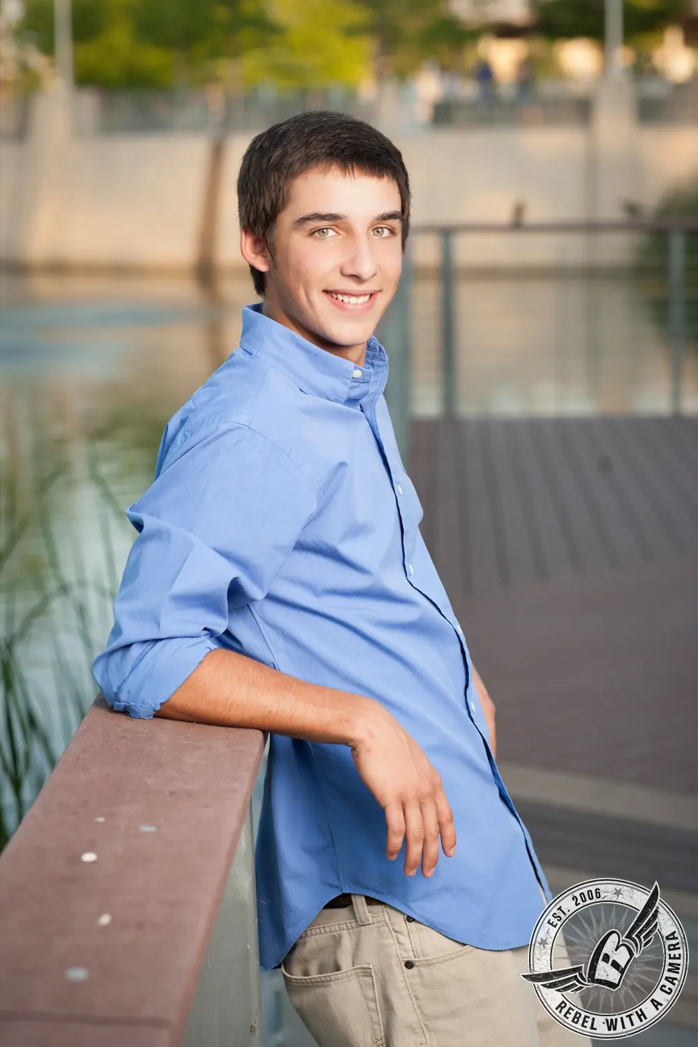 Jacob in a blue button-down shirt leaning on a railing during his senior portrait session.