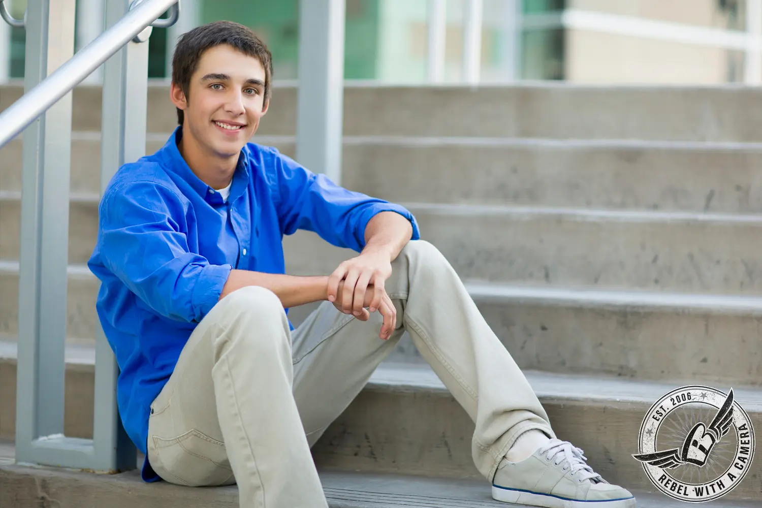 Jacob sits on concrete steps wearing a bright blue shirt, light pants, and white sneakers.