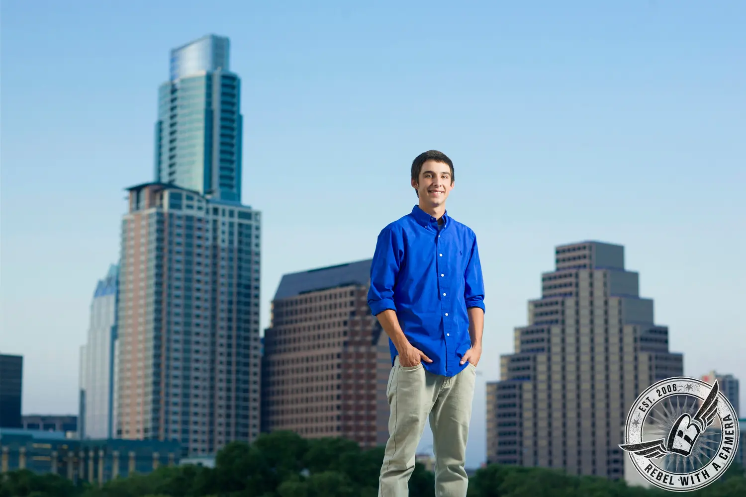 Jacob standing in a blue shirt and light pants with downtown buildings behind him.