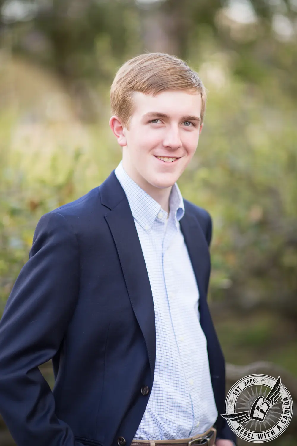 Johnathan wearing a navy blazer and checked shirt in an outdoor senior portrait.