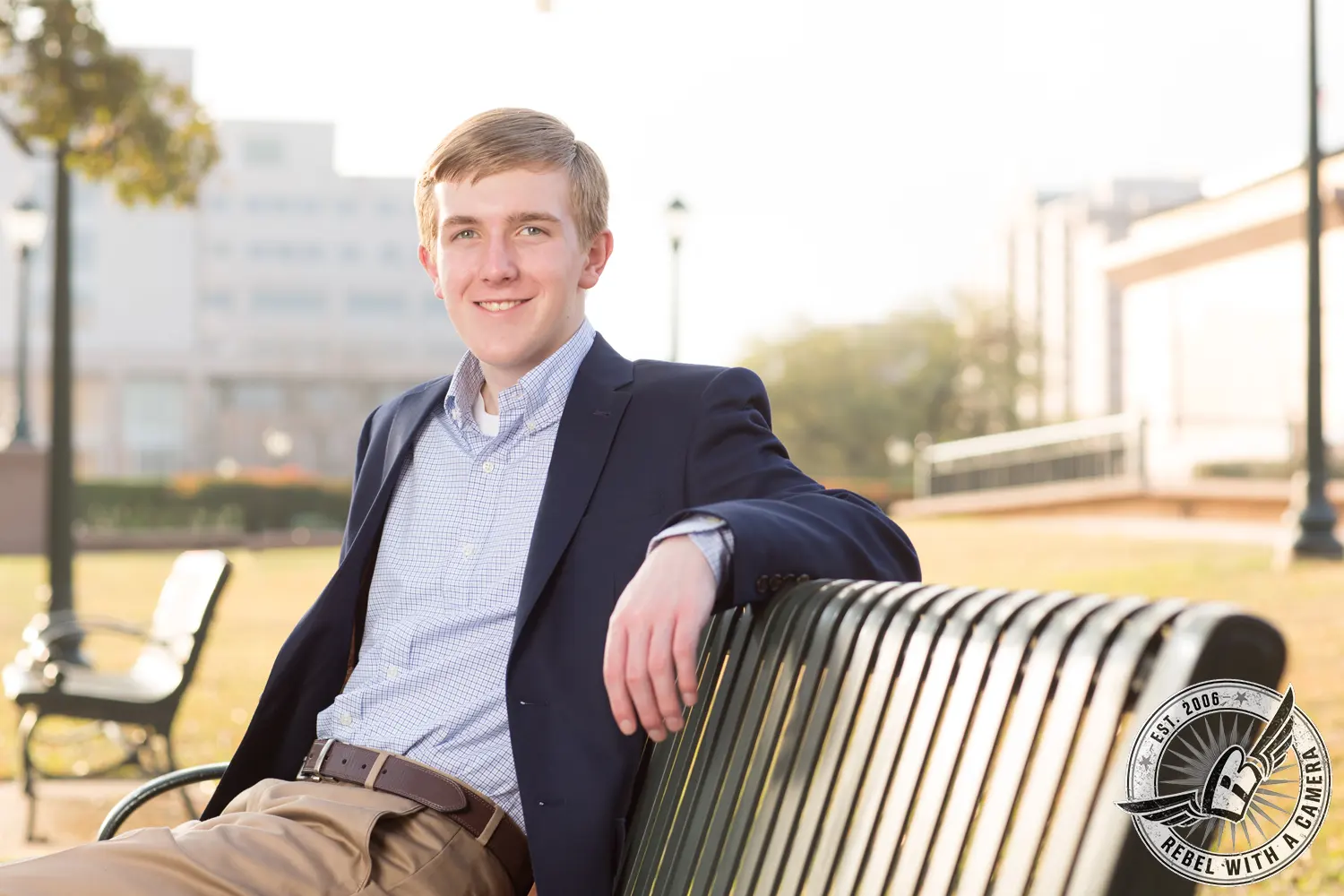 Johnathan, wearing a navy blazer and khaki pants, sits on a metal bench outdoors.