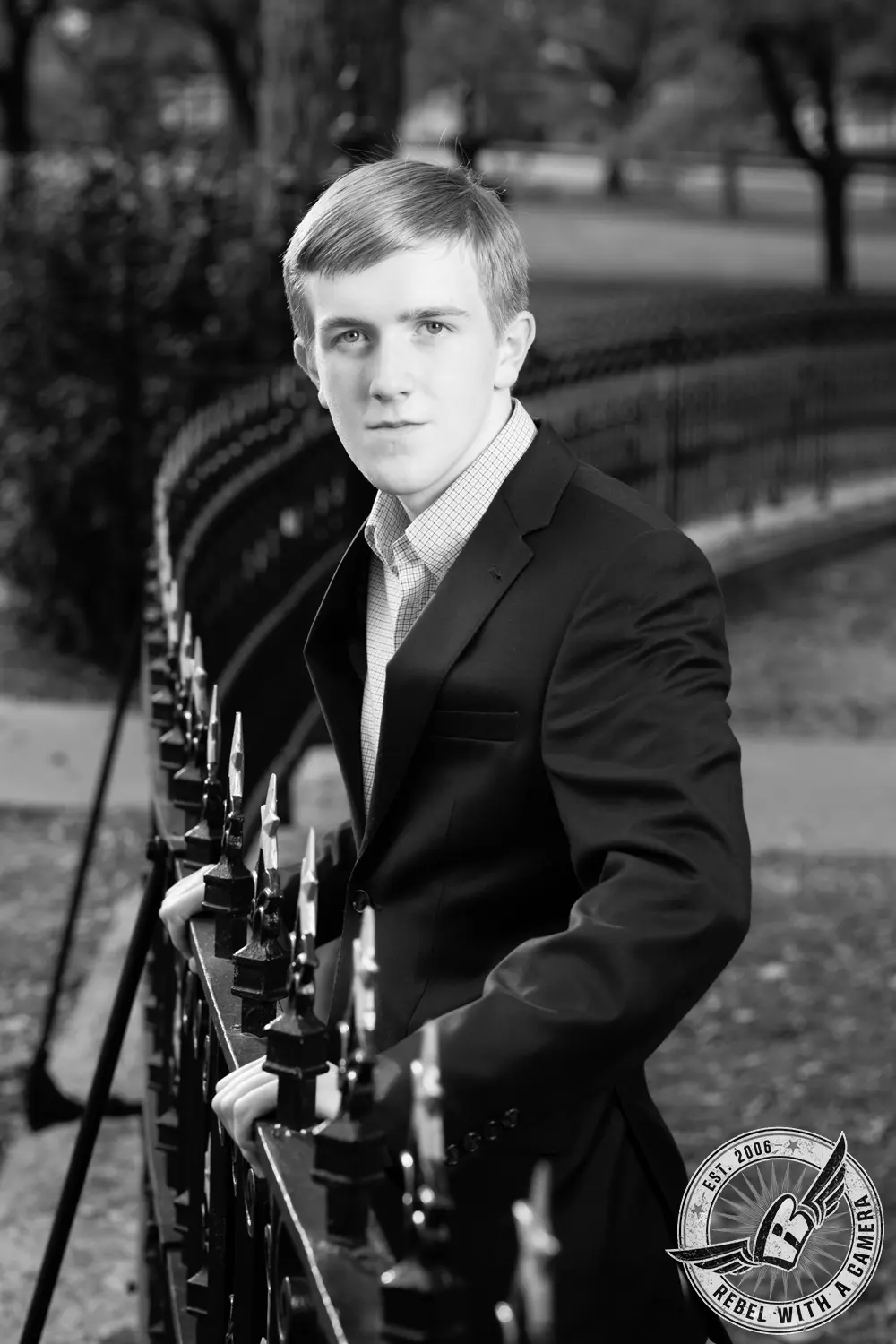 Black-and-white portrait of Johnathan in a dark suit standing beside an ornate iron fence.