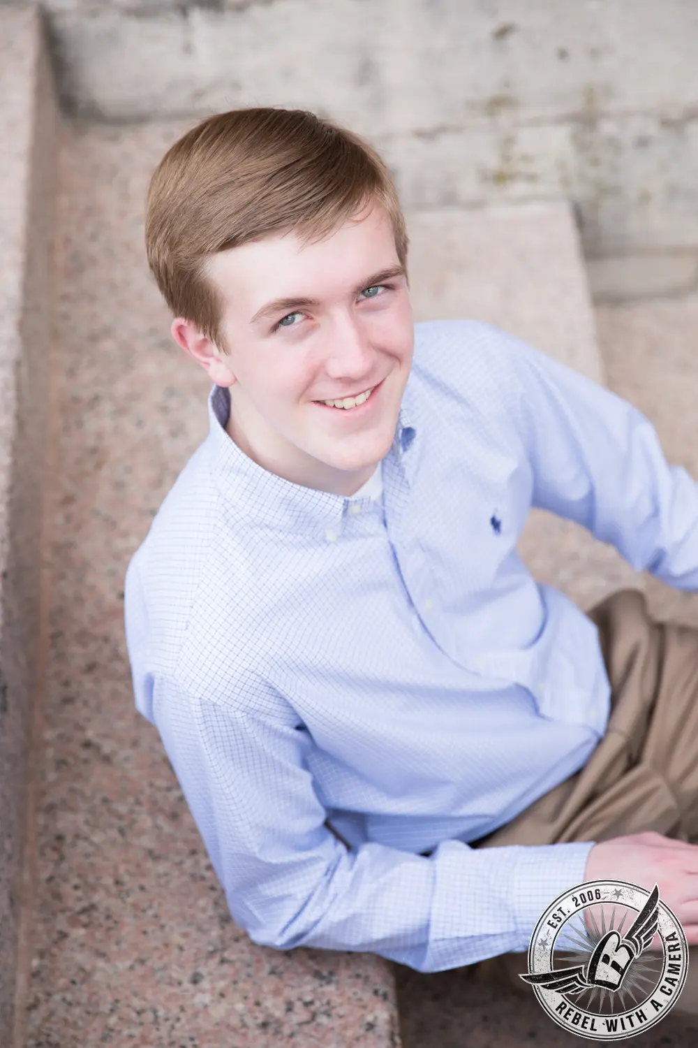 Johnathan seated on stone steps in a light blue button-down shirt and khaki pants, looking up at the camera.