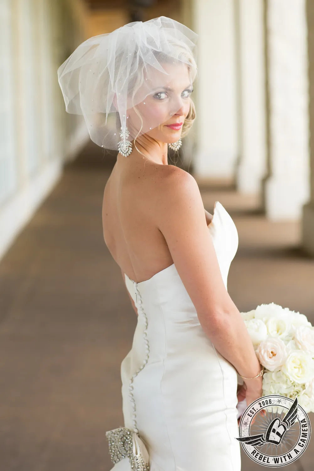 Bride in a veil looking over her shoulder while holding white flowers in Austin, TX.