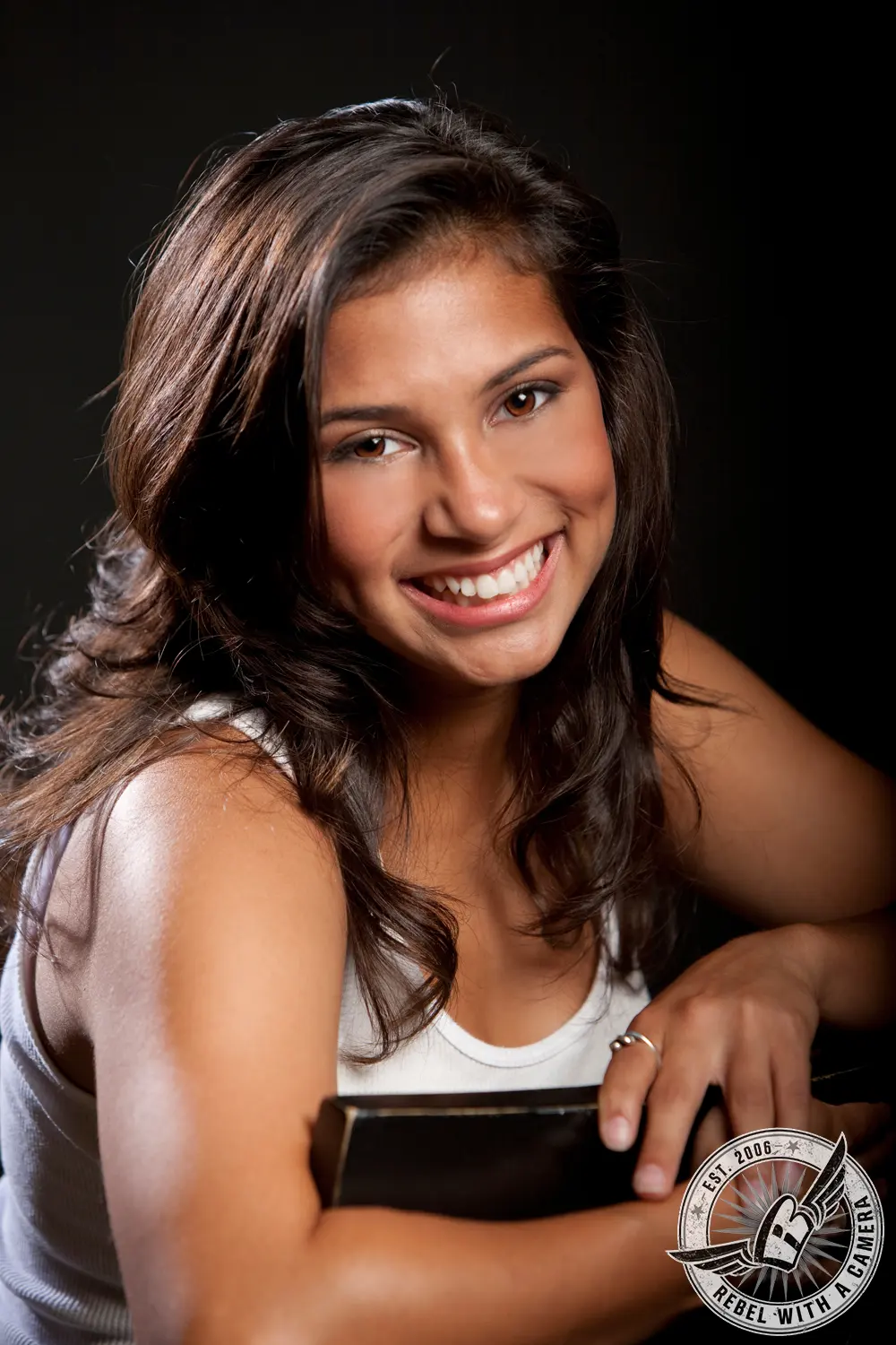 Studio portrait of Katlyn smiling in a white sleeveless top against a black background.