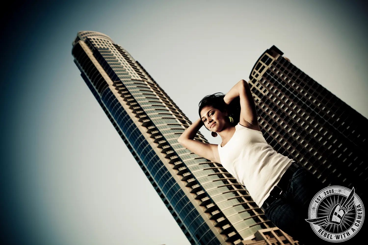 Katlyn poses with her hands behind her head in front of two tall downtown Austin buildings.