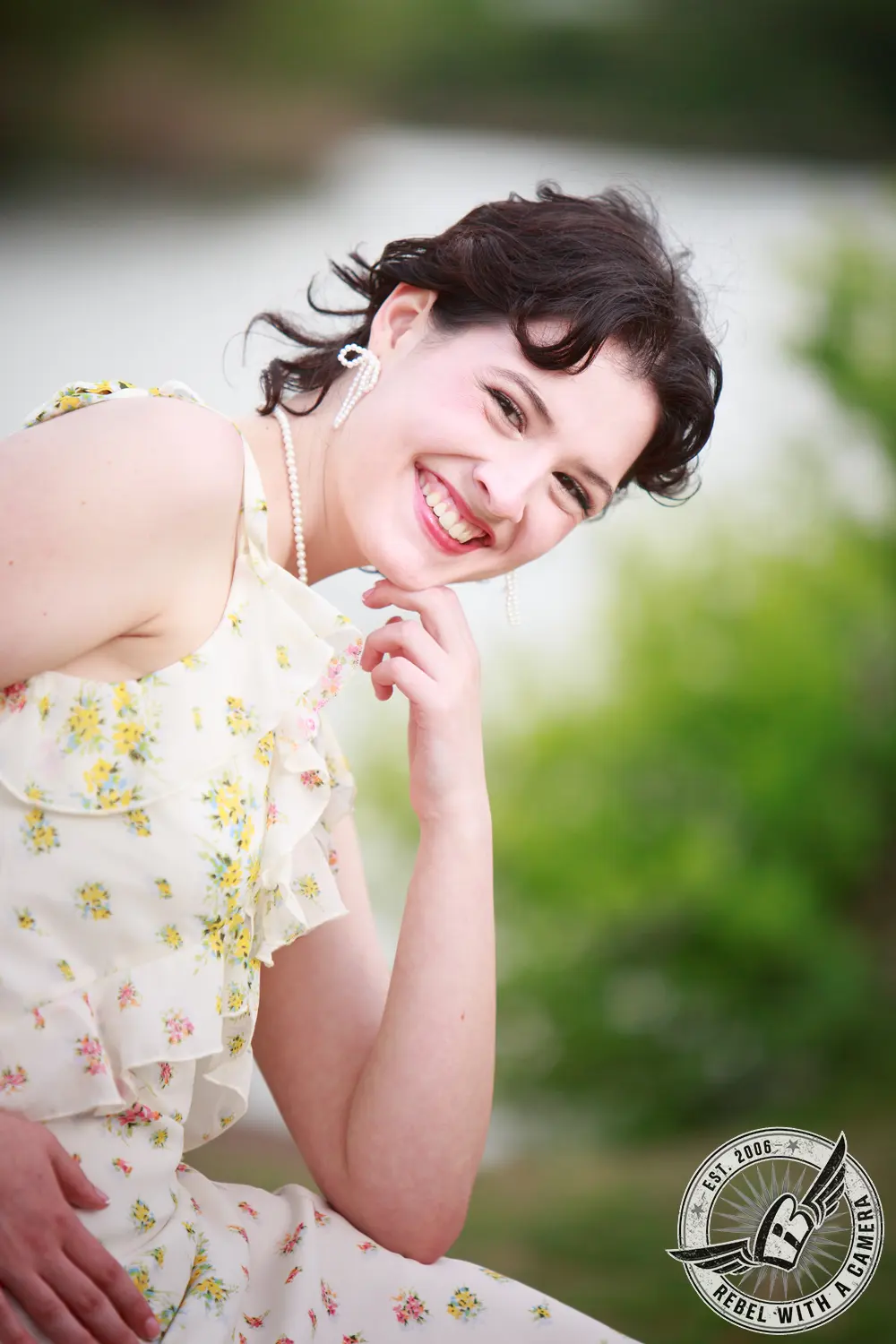 Close-up senior portrait of Liz in a white floral dress with pearl jewelry, posed outdoors.