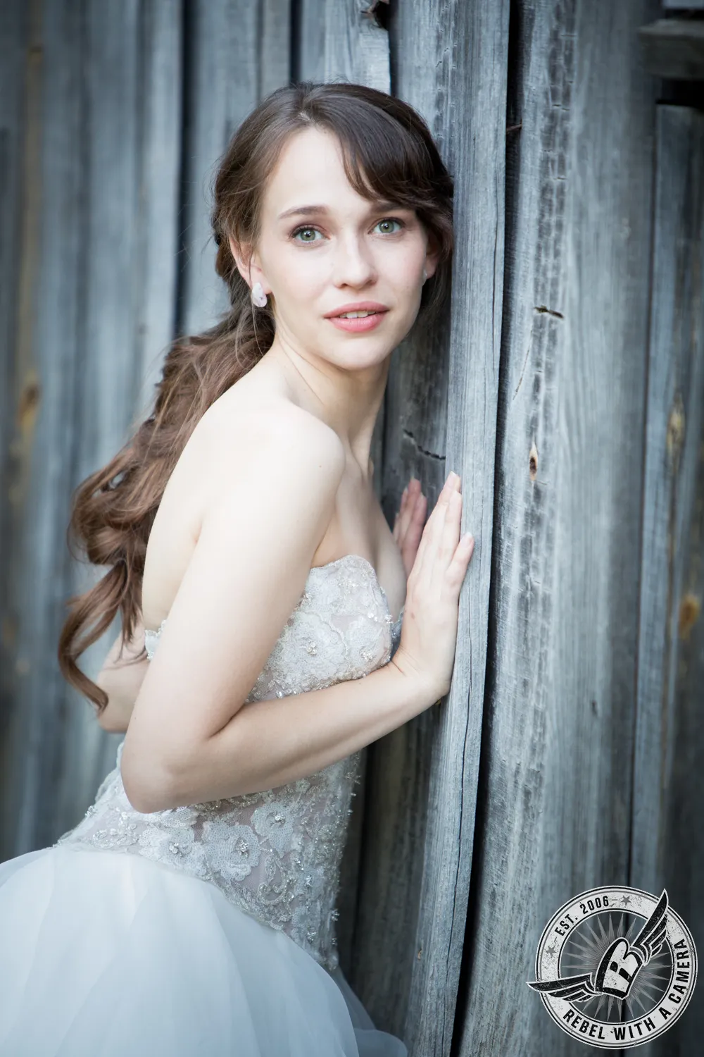 Bride in a wedding dress posing beside a weathered wooden wall