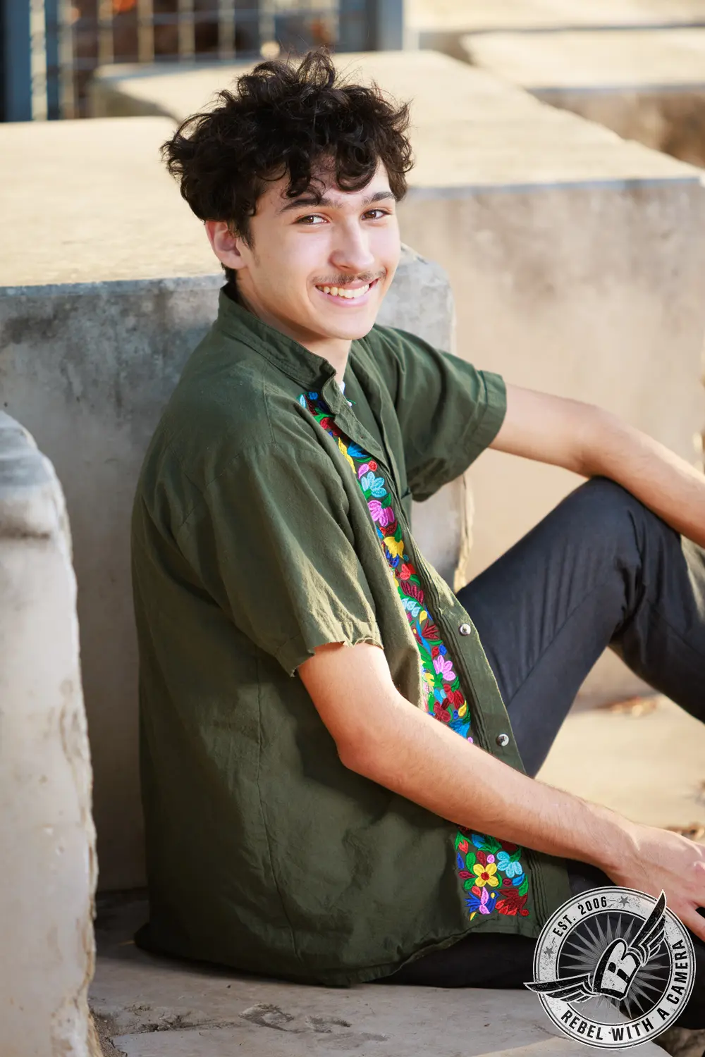 Nathan sits on concrete steps wearing a green shirt with colorful floral embroidery.
