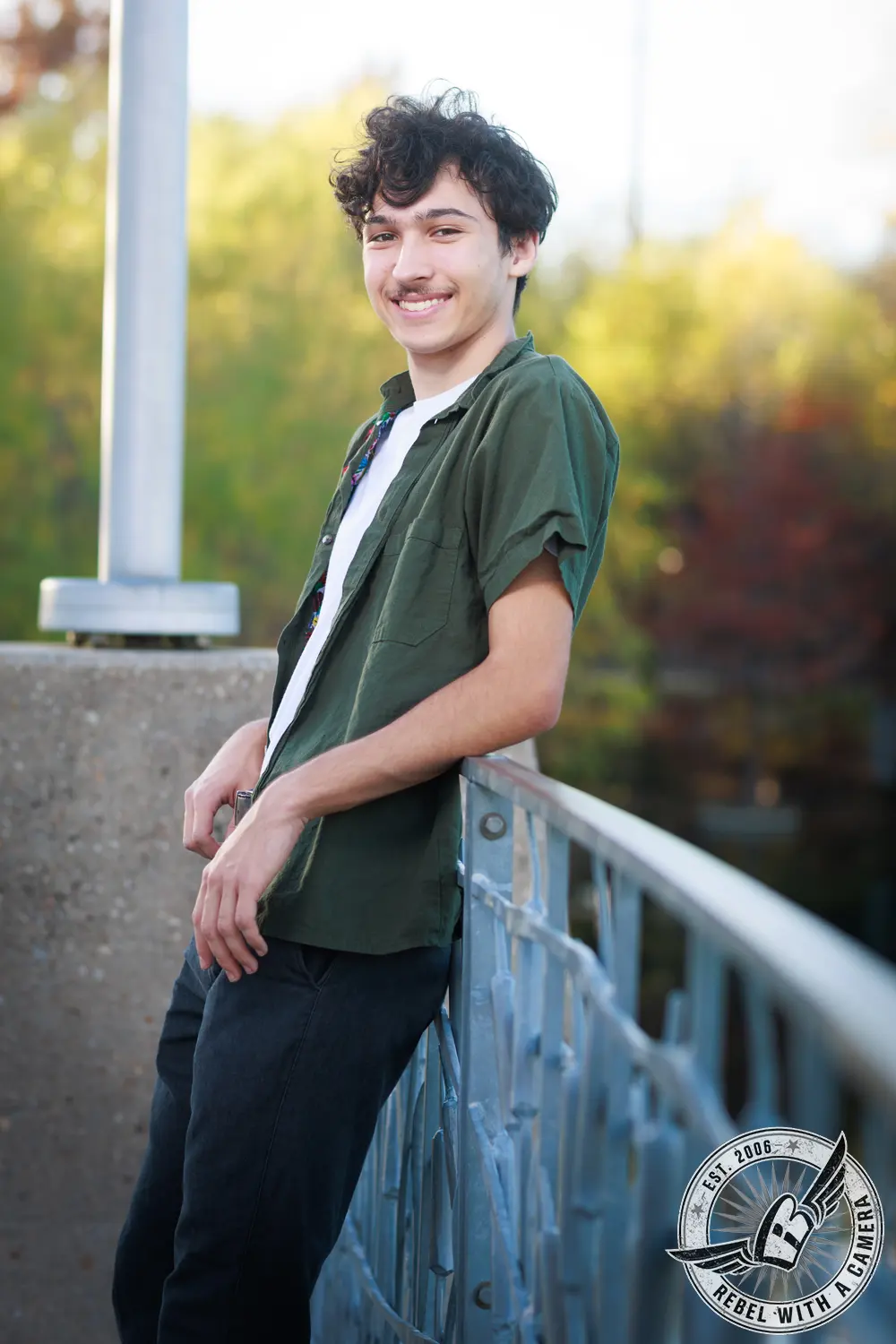 Nathan smiling while leaning against a blue metal railing beside the water.
