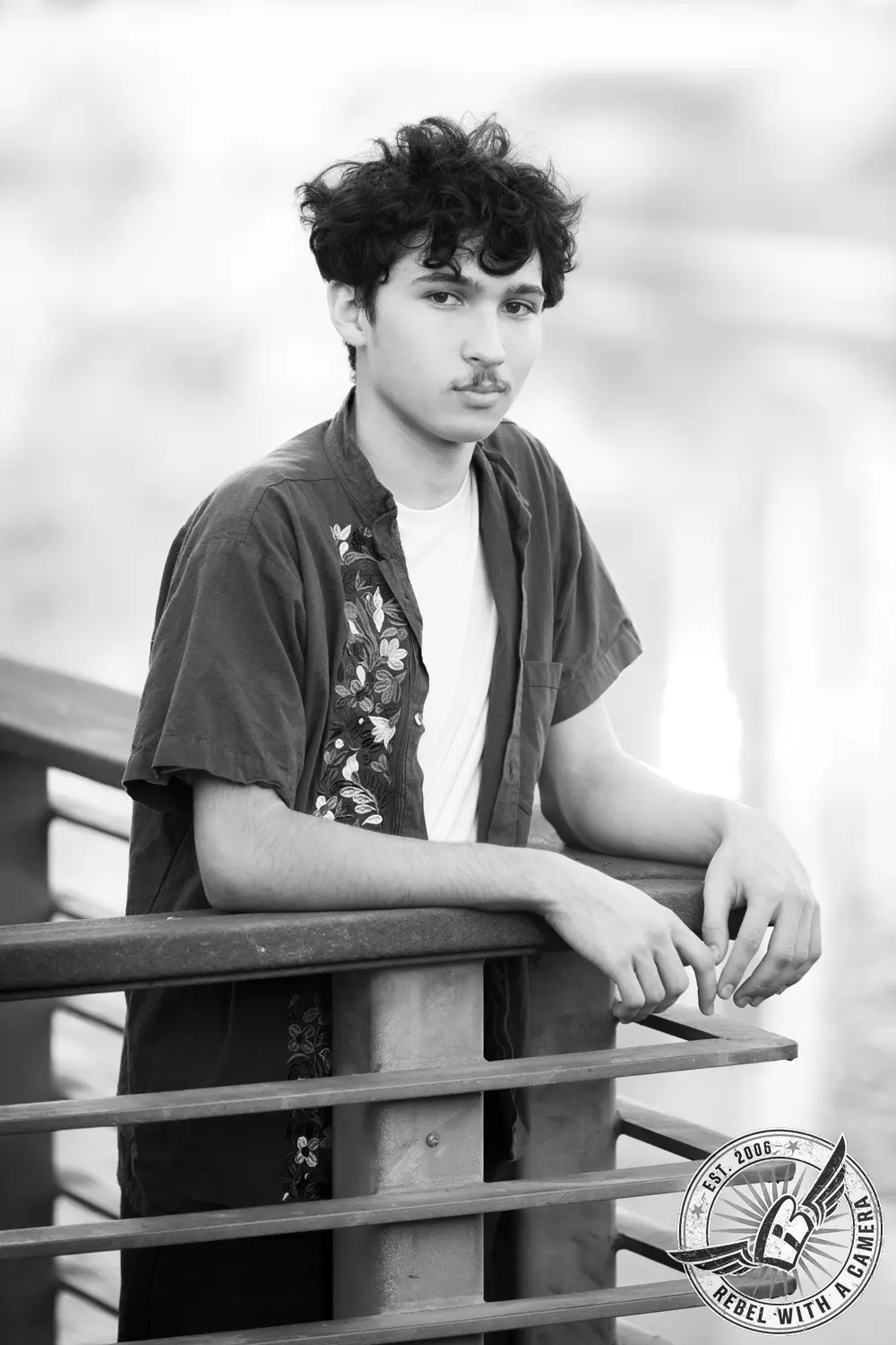 Black-and-white portrait of Nathan leaning on a metal railing beside the water.