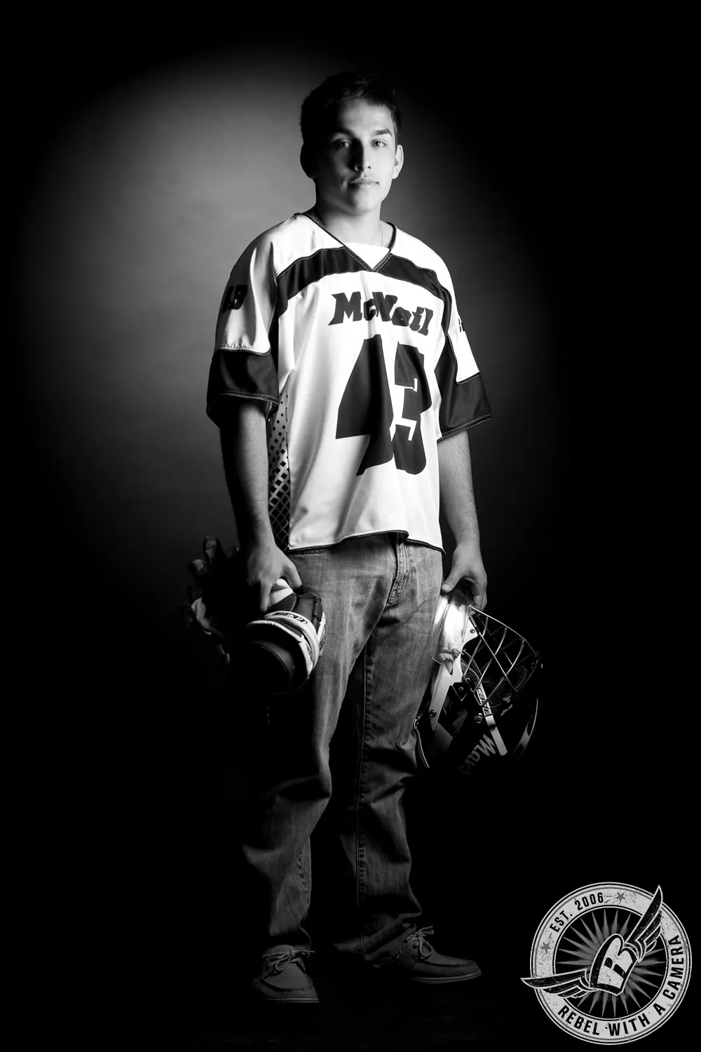 Black-and-white full-length studio portrait of Nick wearing a hockey jersey and holding a hockey glove and goalie mask.
