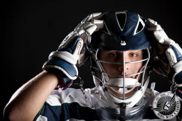 Close-up studio portrait of Nick wearing a hockey helmet, gloves, and jersey against a black background.