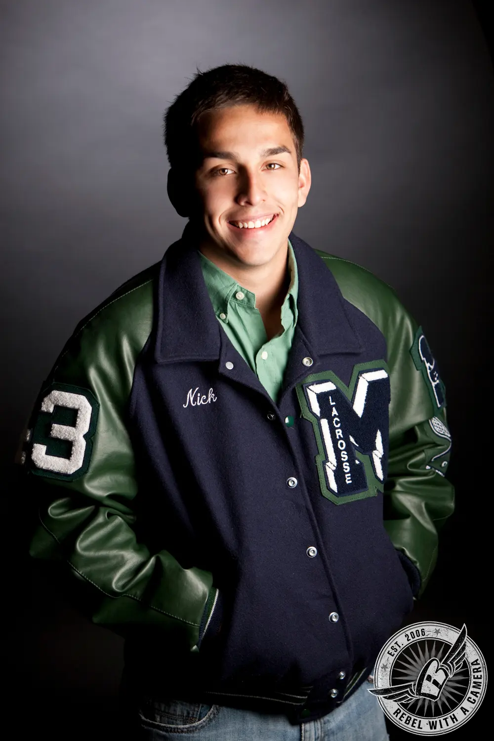 Studio portrait of Nick wearing a green and navy letterman jacket with lacrosse patches.