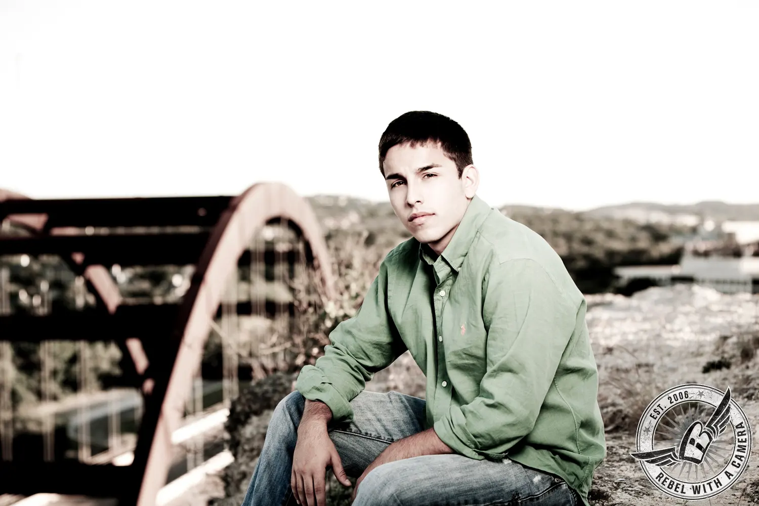 Nick seated outdoors in a green button-down shirt and jeans with Pennybacker Bridge behind him.