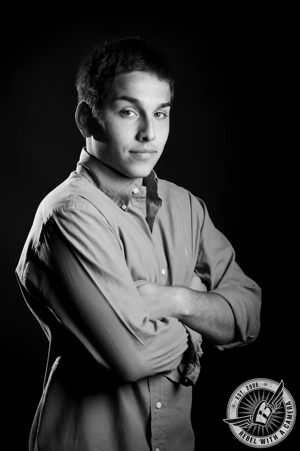 Black-and-white studio portrait of Nick standing with his arms crossed against a dark background.
