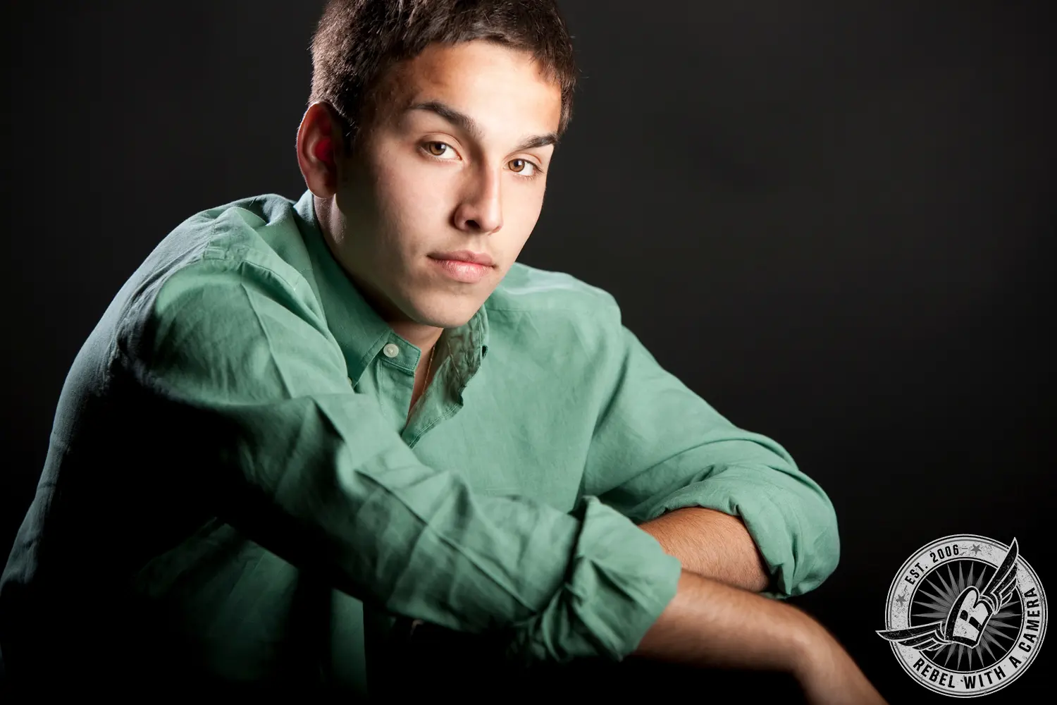 Studio portrait of Nick in a green button-up shirt against a dark background.