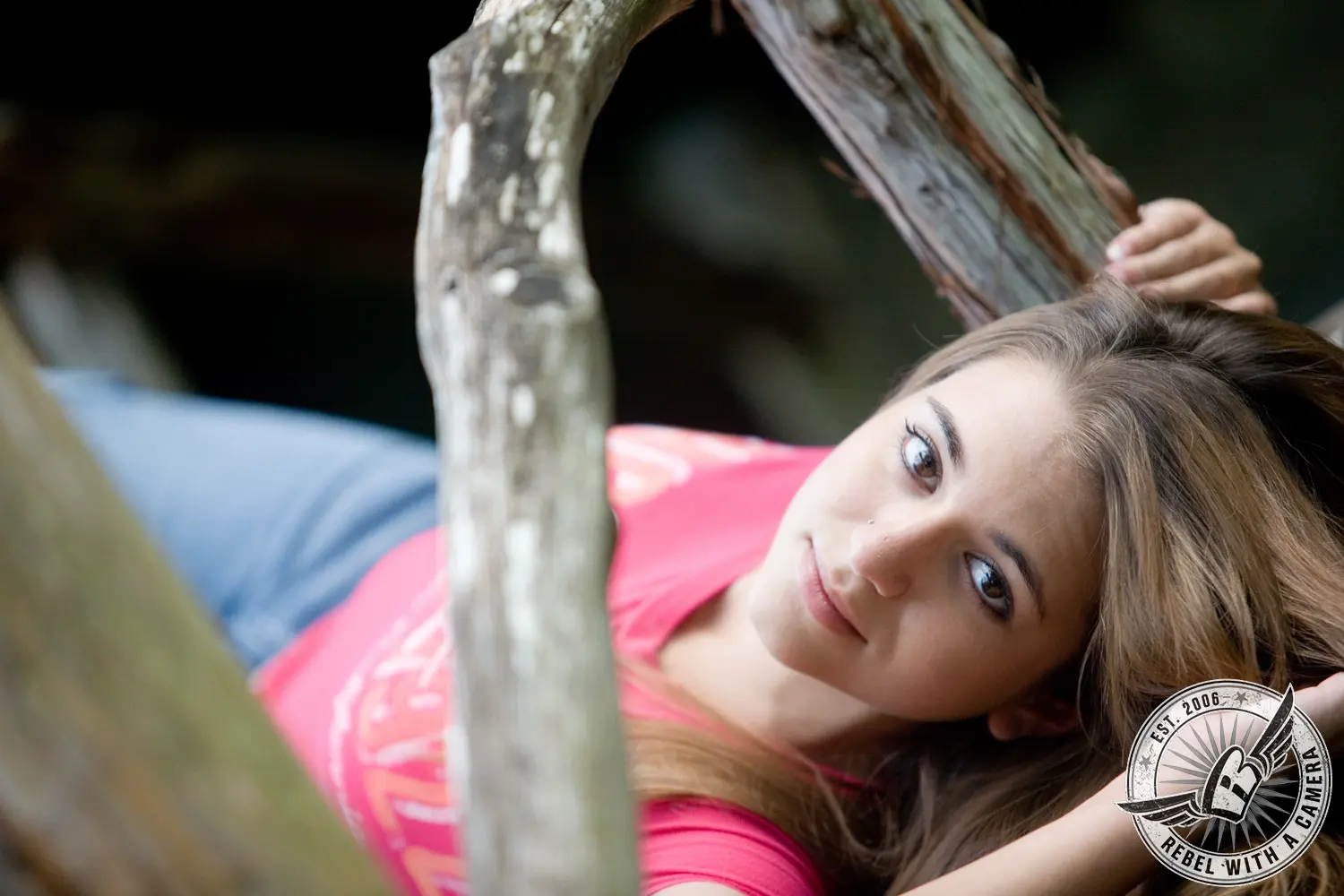 Ruby reclines among pale tree branches wearing a bright pink top and blue jeans.