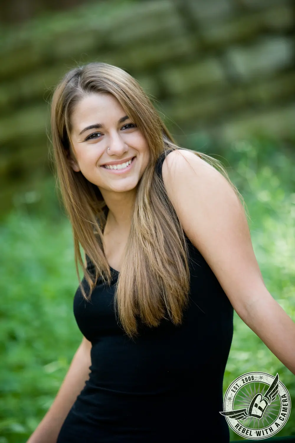 Ruby smiling in a black sleeveless dress against a softly blurred green garden background.