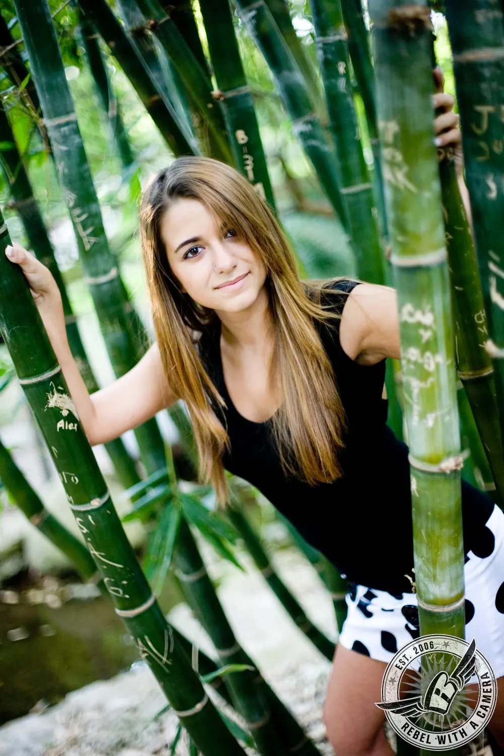 Ruby stands among tall green bamboo stalks, wearing a black top and patterned white shorts.