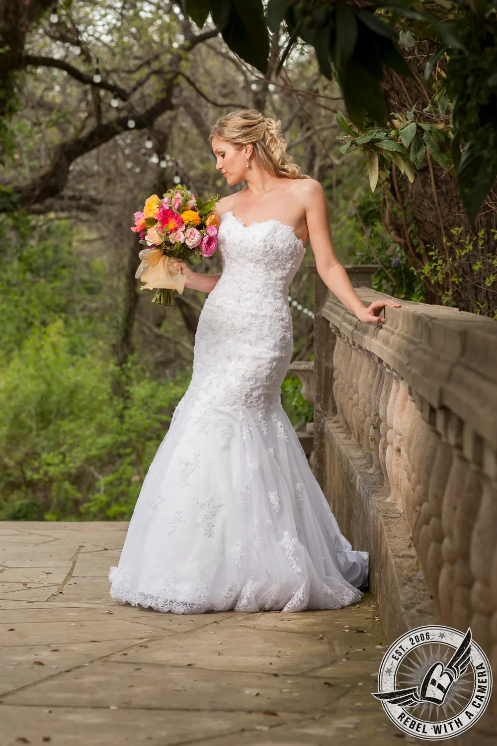 Bride in a lace wedding dress holding a colorful bouquet on a garden bridge in Austin, TX.
