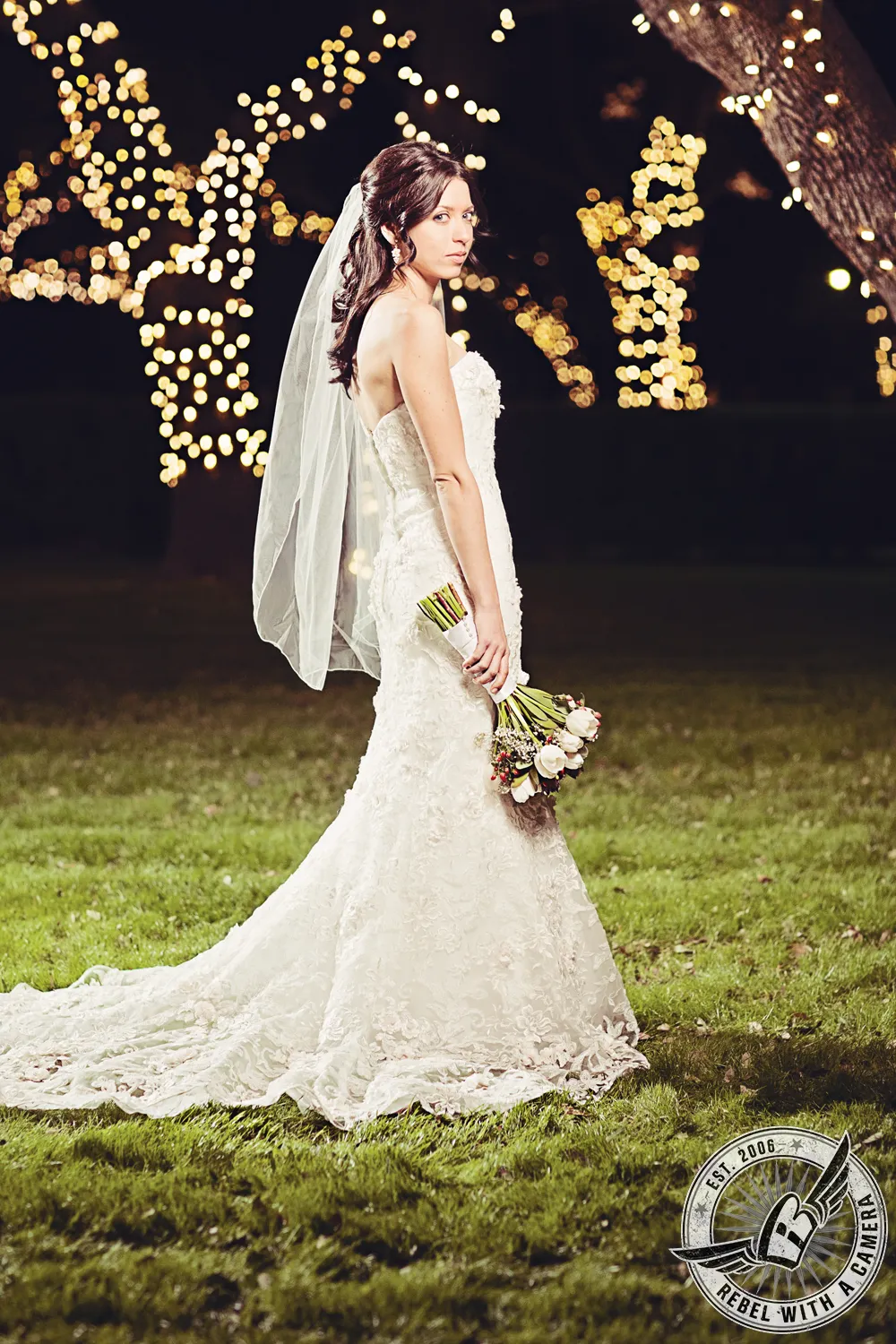 Bride in a lace wedding dress holding a bouquet among outdoor lights