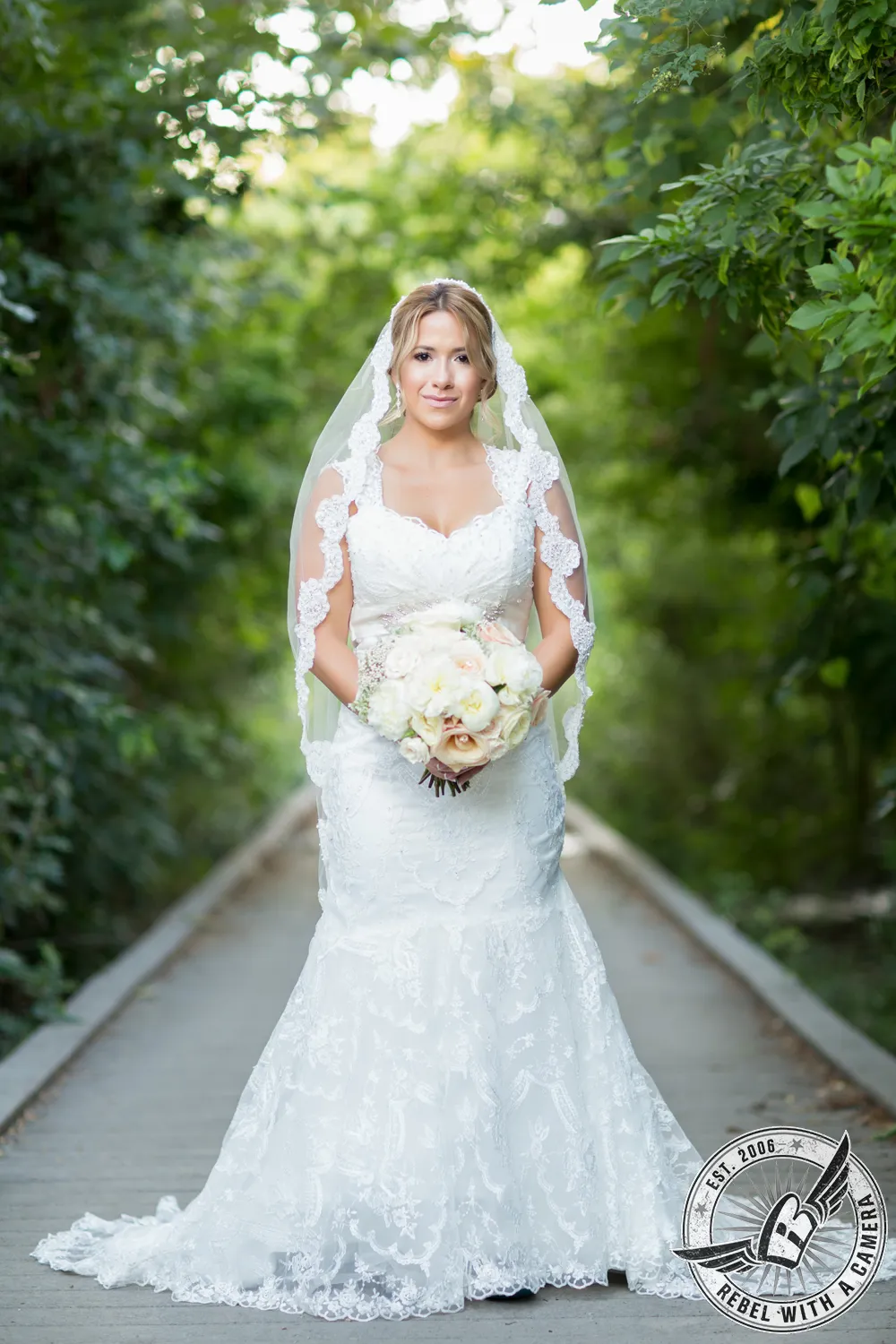 Bride in a lace wedding dress holding a bouquet on a garden path