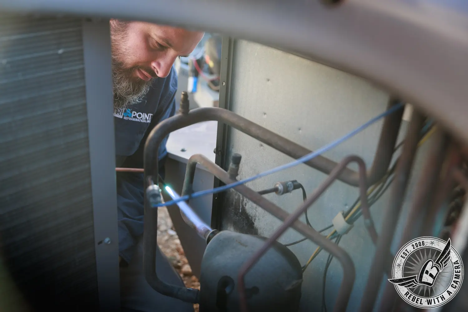 Tri-Point Refrigeration technician inspecting piping and components inside a commercial HVAC unit.