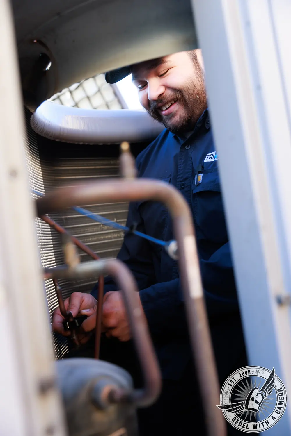 Tri-Point Refrigeration technician working inside an HVAC unit among copper pipes and condenser coils.