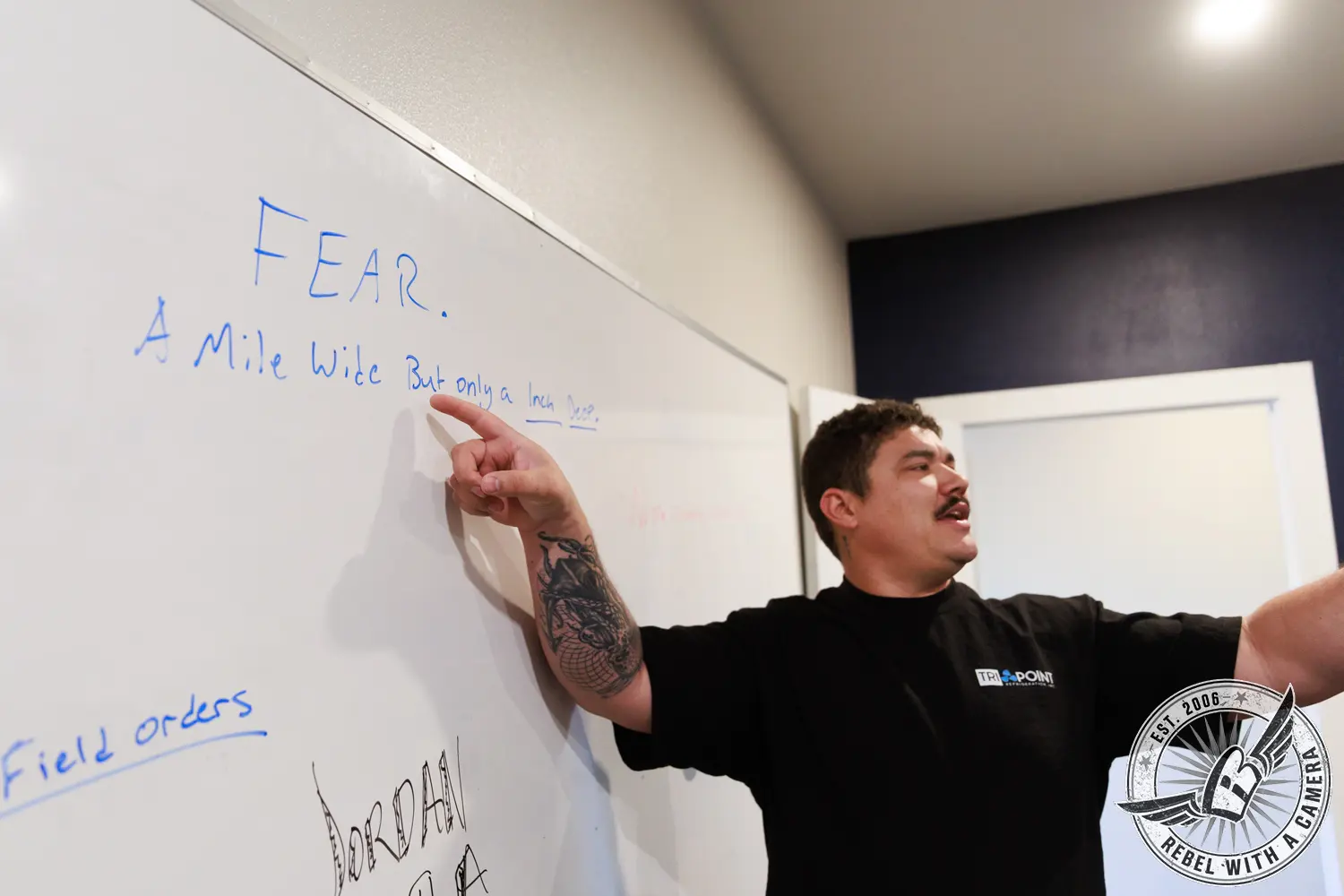 Tri-Point Refrigeration employee gestures beside a whiteboard with handwritten notes.